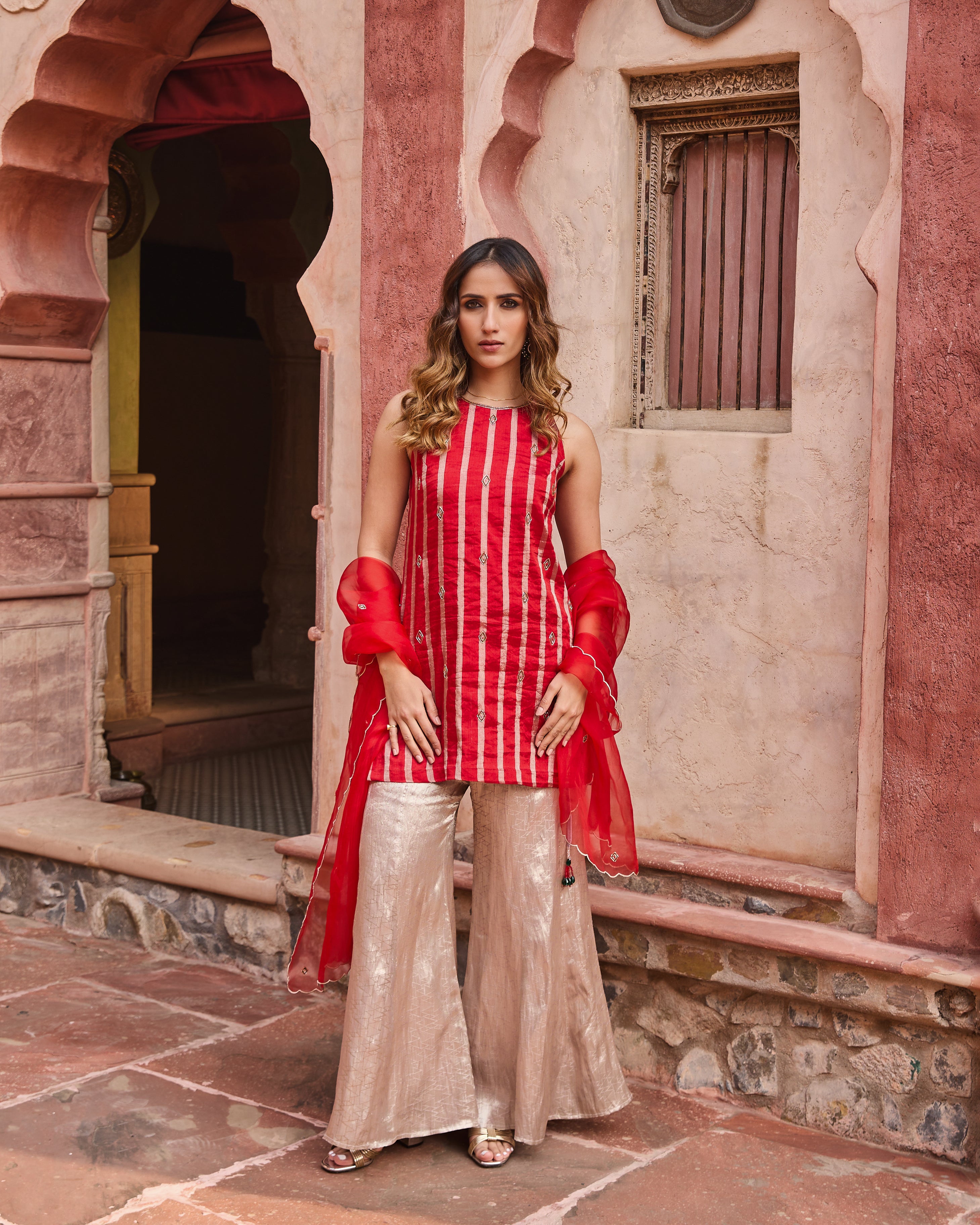 A woman wearing a red and silver straight short kurti with cut-dana embroidery and a keyhole back, paired with a silver chandni sharara and an organza dupatta with scalloped edges.